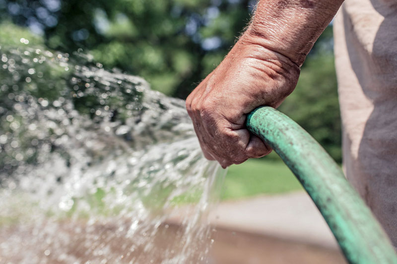 A hand holding a running garden hose with water spraying.