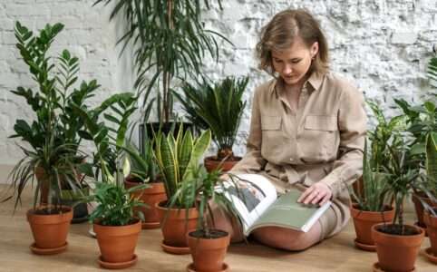 Woman in brown button-up shirt surrounded with plants, reading book.