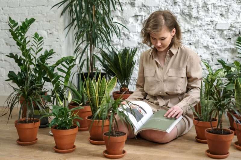 Woman in brown button-up shirt surrounded with plants, reading book.