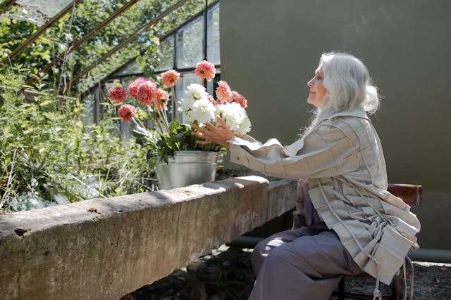 Woman arranging flowers in a garden surrounded by greenery and natural light.